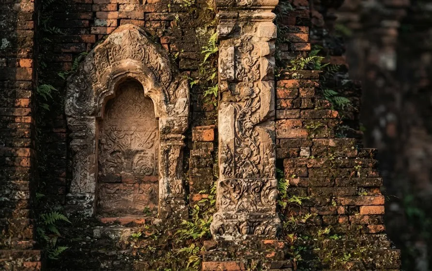 Close-up of a weathered brick temple wall with a carved sandstone niche and floral scroll ornament