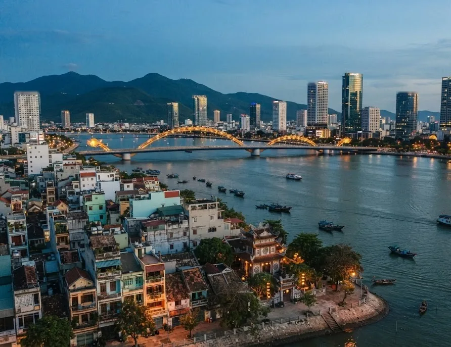 River city skyline at dusk with old tube houses, a pagoda, arched bridges and modern towers