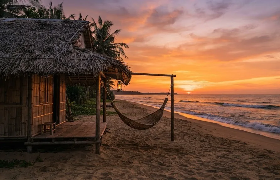 Thatched beach hut with a hammock and lantern at an orange sunset over the sea