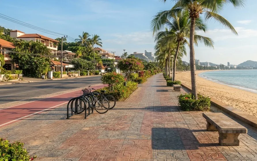 Wide tiled beach promenade with palms, benches, a red bike lane and parked bicycles beside the sand