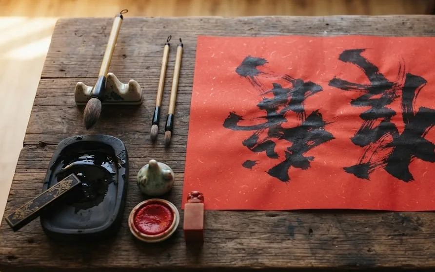 Brushes, ink slab, seal and red paper with bold black brush strokes on a dark wooden table