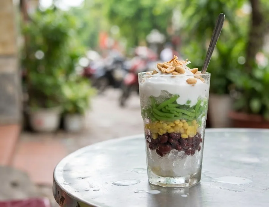 A tall glass of layered Vietnamese che dessert on a metal table at a street stall
