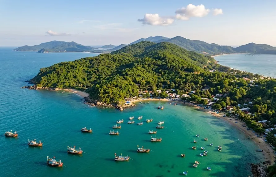 Aerial view over a forested peninsula and a bay with fishing boats