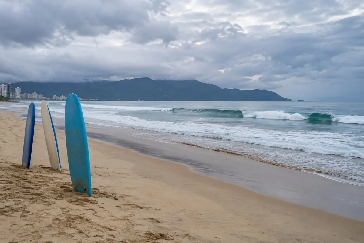 Clean waves rolling onto a long sandy beach with surfboards in the sand on a cloudy day