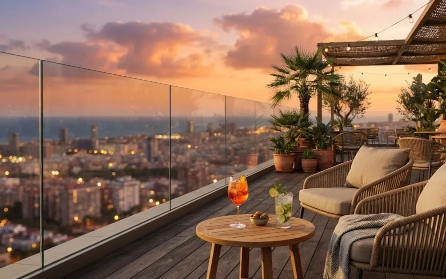 Rooftop terrace with rattan lounge chairs, palms and cocktails overlooking a coastal city at sunset