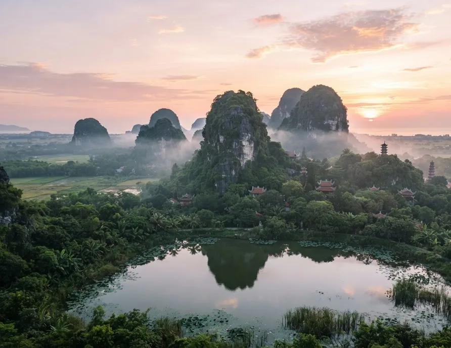 Misty limestone peaks and pagodas reflected in a pond at sunrise