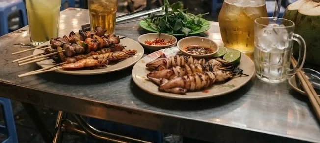 Grilled skewers and squid with iced tea, sugarcane juice and a coconut at a street table