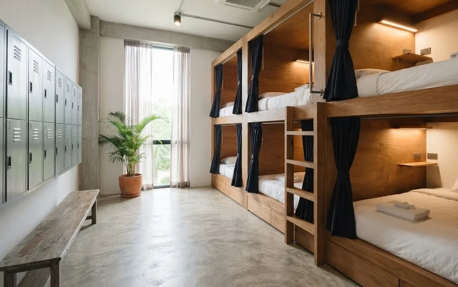 Dormitory room with timber capsule bunks, privacy curtains, reading lamps and a row of lockers