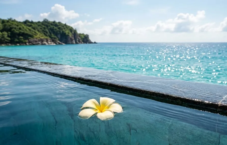 Close-up of an infinity pool edge with a floating frangipani blossom merging into the turquoise sea