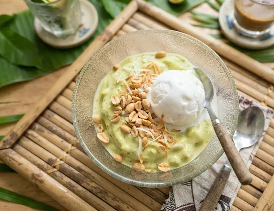 A glass bowl of Vietnamese avocado ice cream topped with coconut ice cream and peanuts