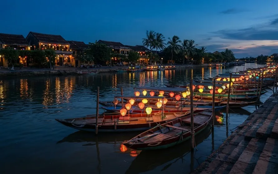 Wooden rowing boats hung with glowing silk lanterns moored on a calm river at blue hour