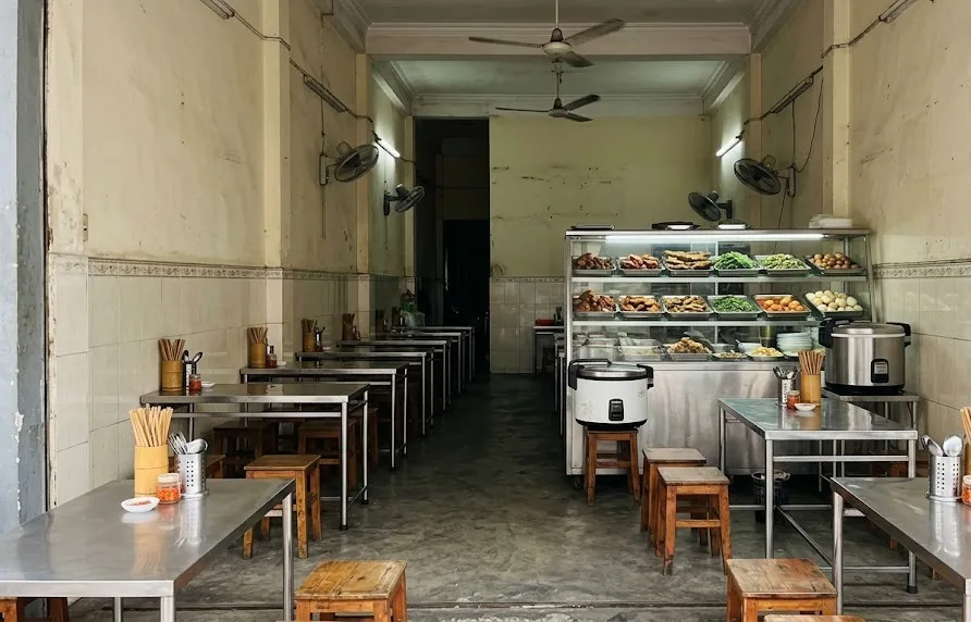 Empty Vietnamese lunch eatery with steel tables, stools and a glass counter of home-style dishes