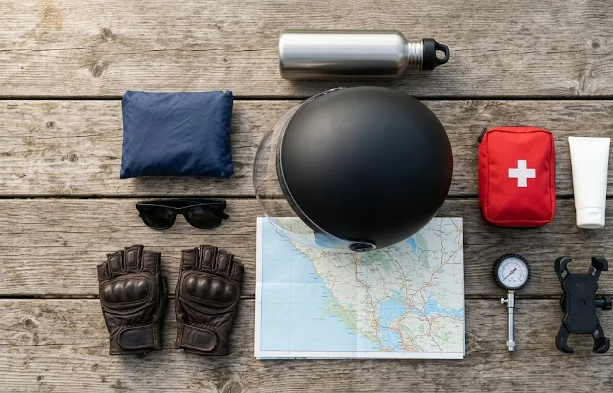 Flat lay of motorbike trip essentials: helmet, gloves, rain poncho, map, first aid kit, bottle and tyre gauge