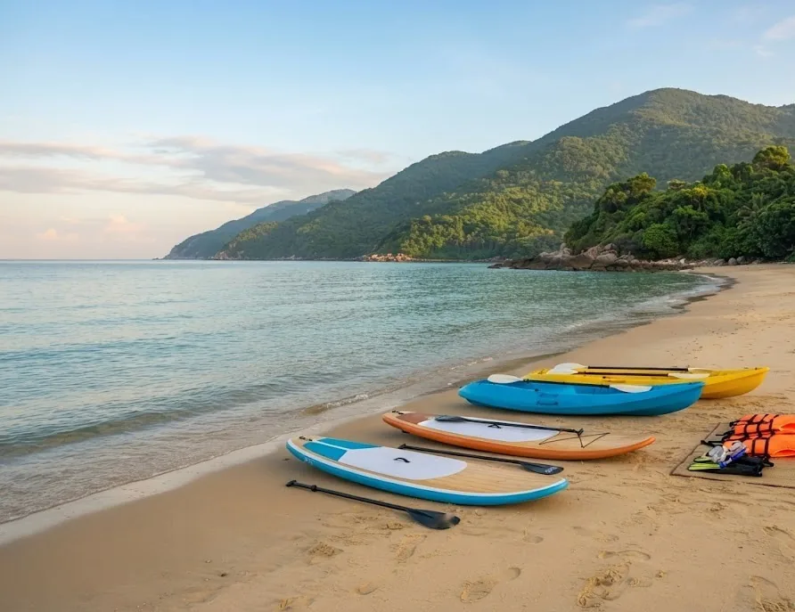 Paddle boards, kayaks and life vests on a quiet beach below green hills