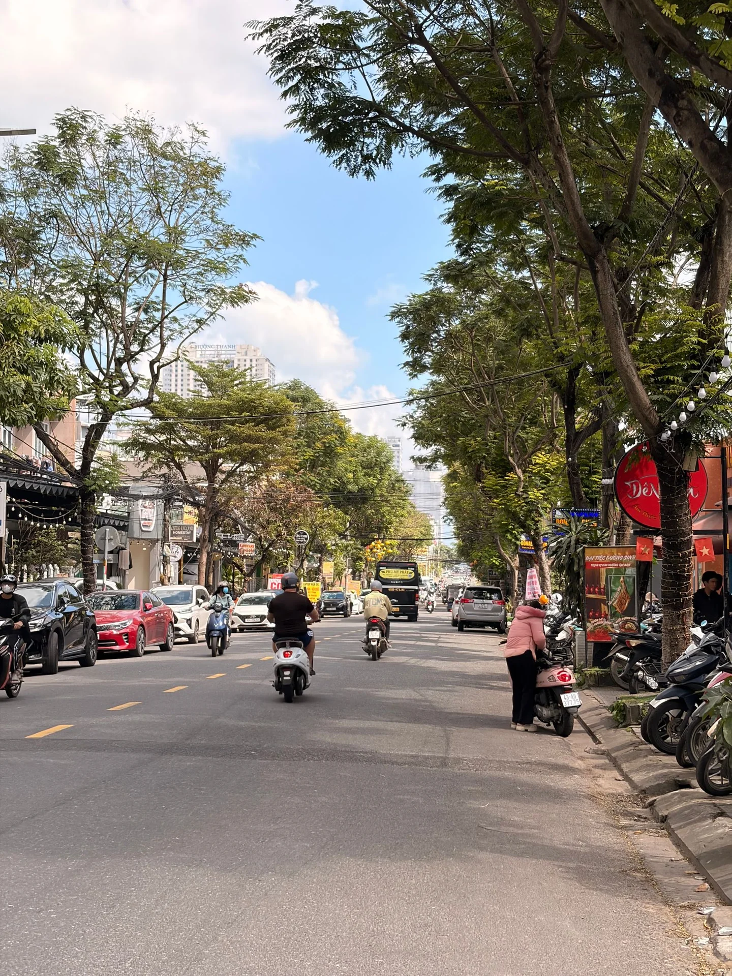 Tree-lined street with motorbikes and shops in Da Nang city