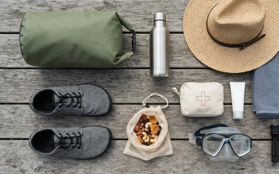 Flat-lay of a dry bag, water bottle, reef shoes, straw hat, towel, first-aid pouch and snorkel mask