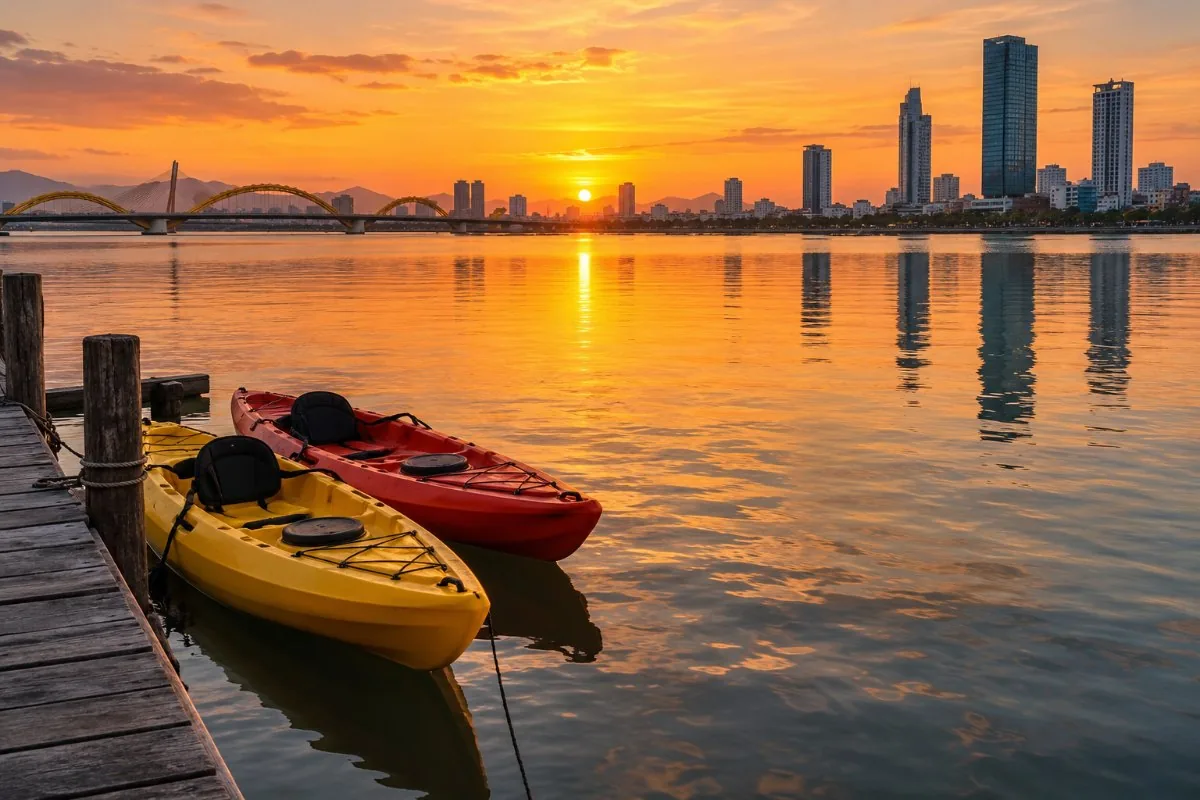 Two kayaks tied to a wooden jetty on a river with the city skyline at sunset
