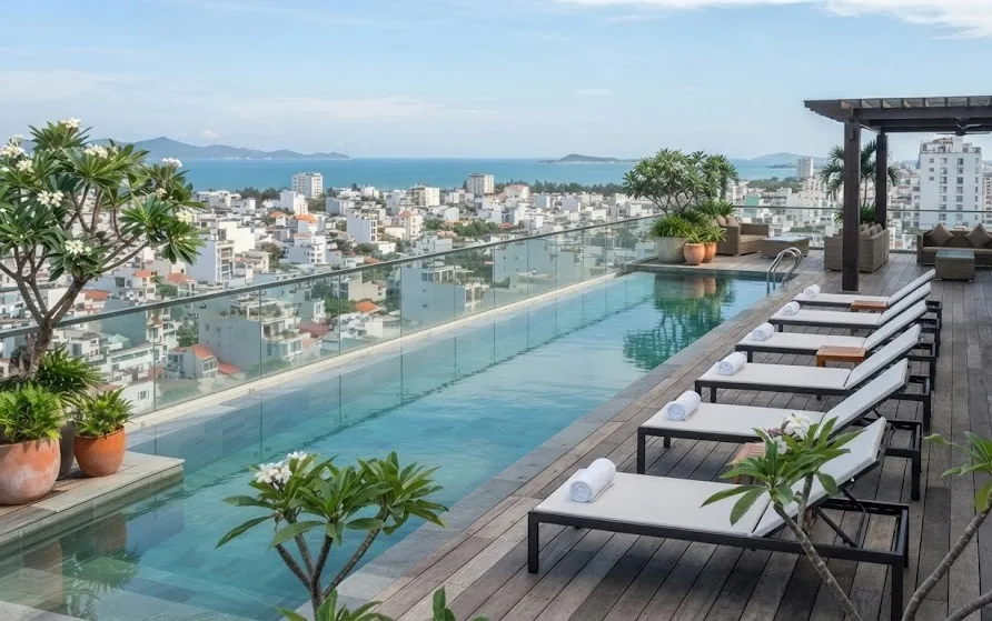 Rooftop pool with a glass edge, timber deck and loungers above a tropical coastal city and the sea