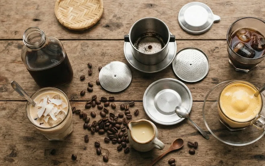 Flat-lay of a disassembled phin filter, iced coffee, egg coffee, coconut coffee, cold brew and roasted beans