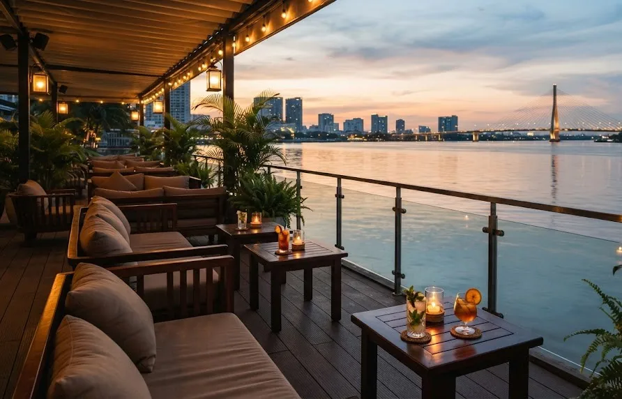 Riverside lounge terrace with sofas, cocktails and candles facing a bridge at sunset