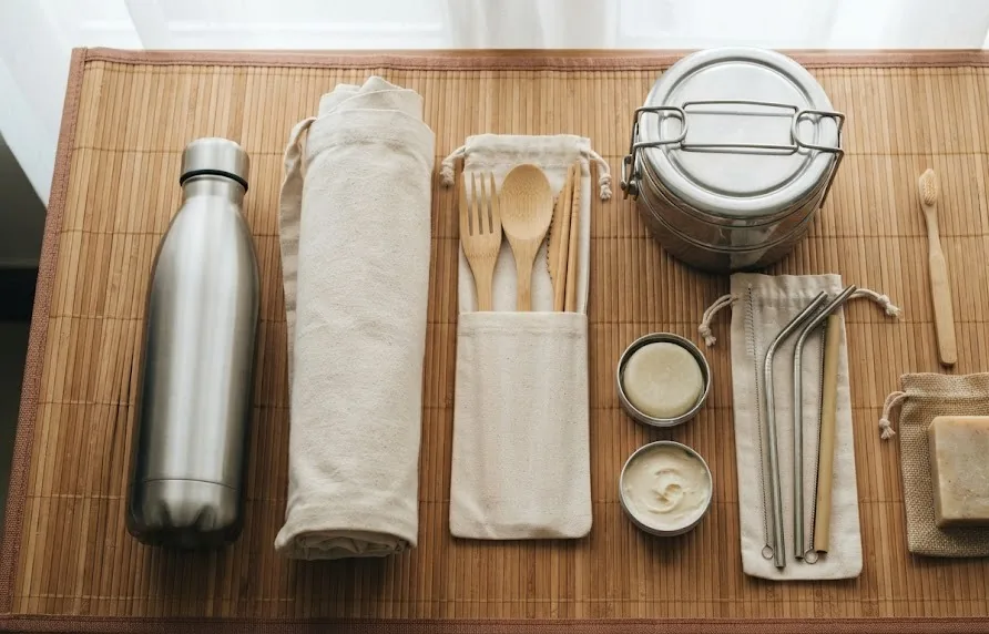 Steel bottle, bamboo cutlery, reusable straws, cloth bag, tiffin tin and solid soap on a bamboo mat