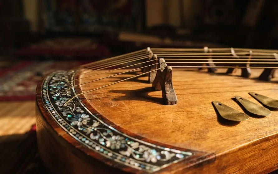Close-up of a wooden zither with brass strings, carved bridges, pearl inlay and finger plectrums